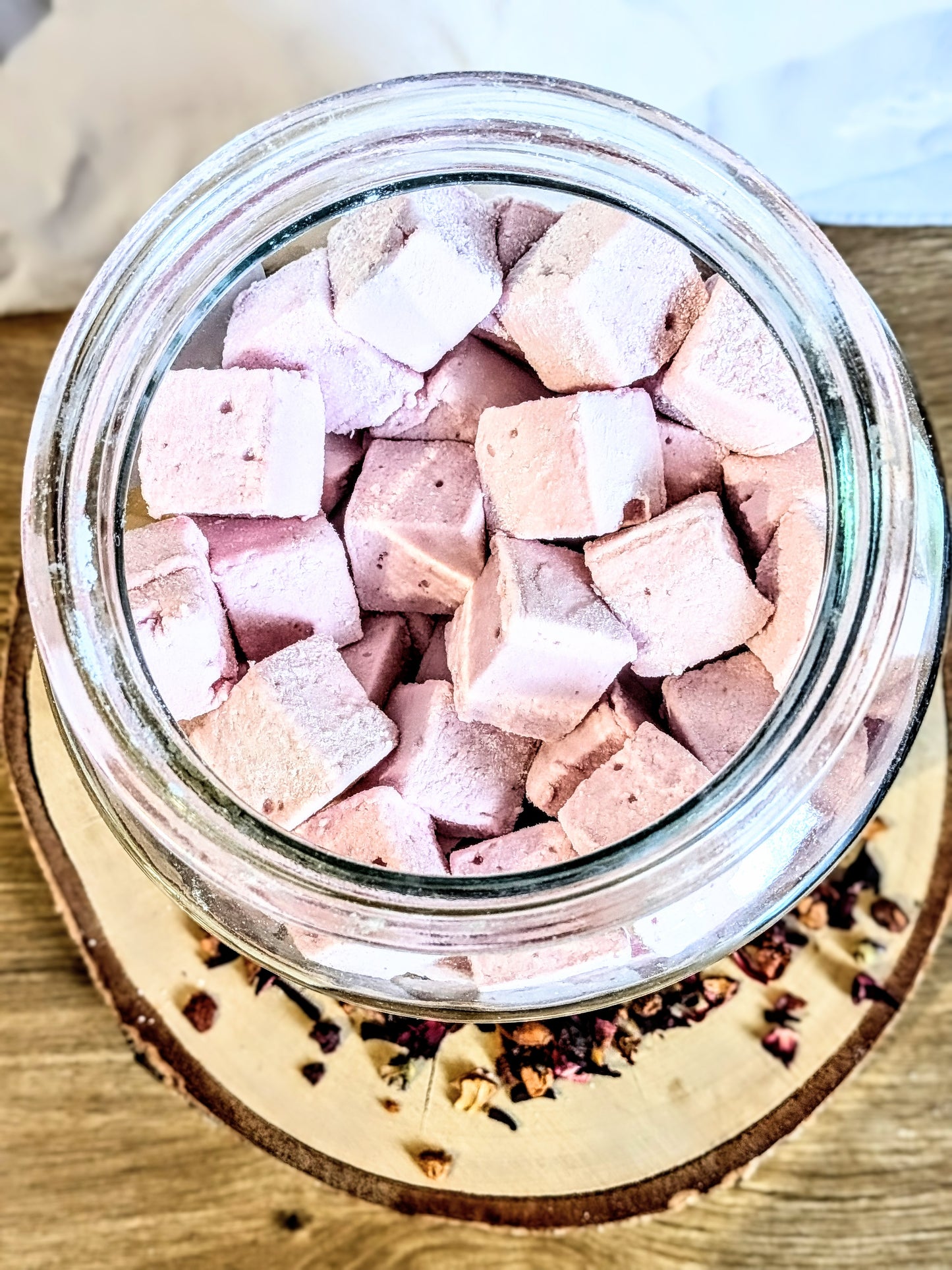 Détail de la texture moelleuse et poudrée de guimauves artisanales à l'infusion de framboise et fruit de la passion, vue de dessus dans un bocal en verre. Guimauve artisanale Orléans.