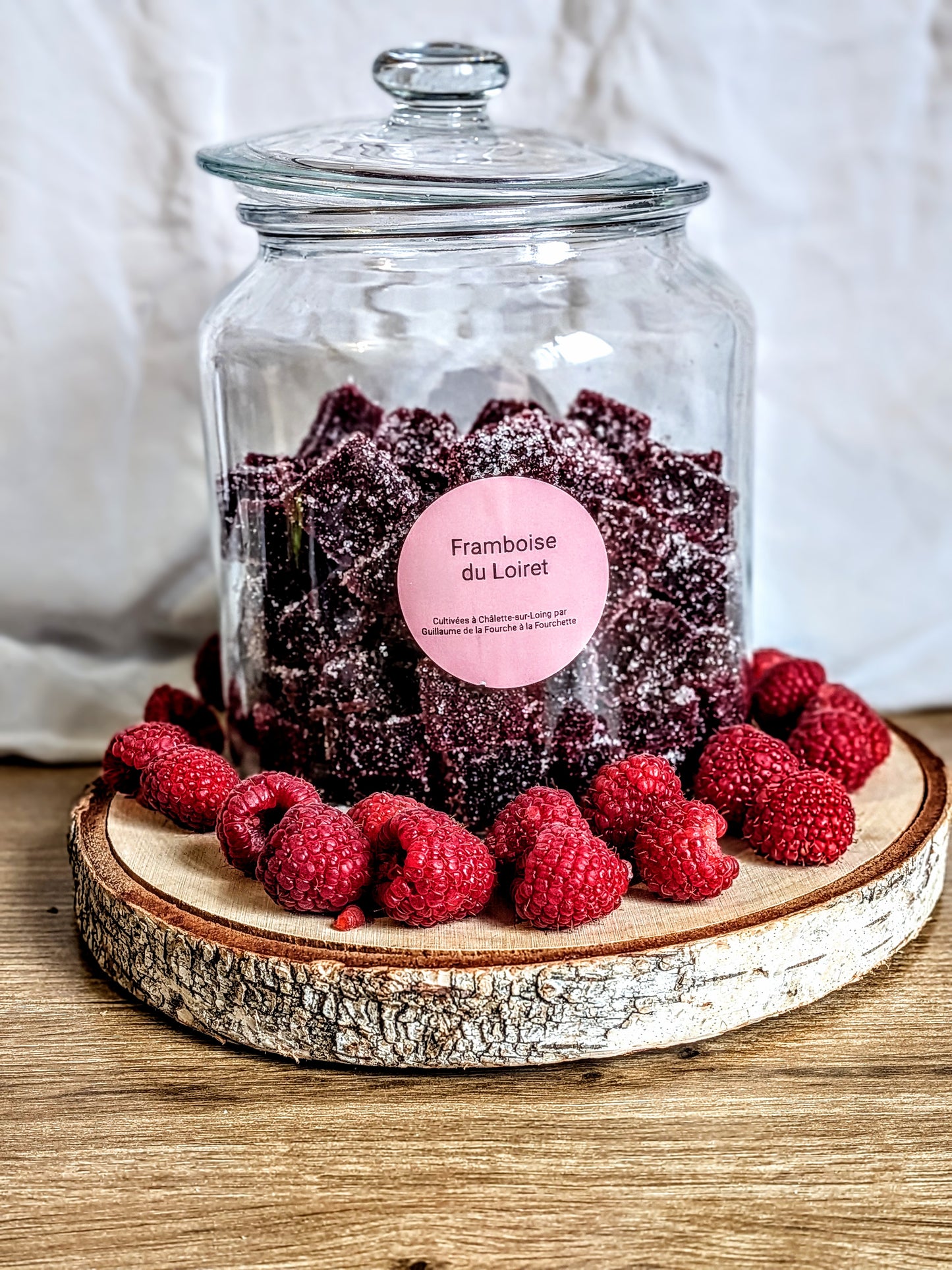 Bocal en verre rempli de pâtes de fruits à la framboise, étiquette Framboise du Loiret, sur support en bois