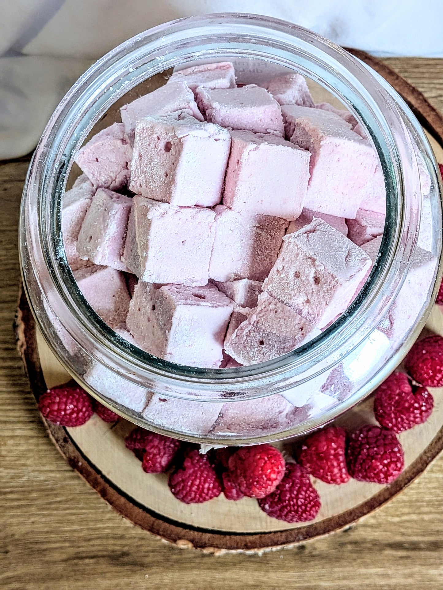 Vue plongeante dans un bocal de guimauves roses à la framboise entouré de fruits frais