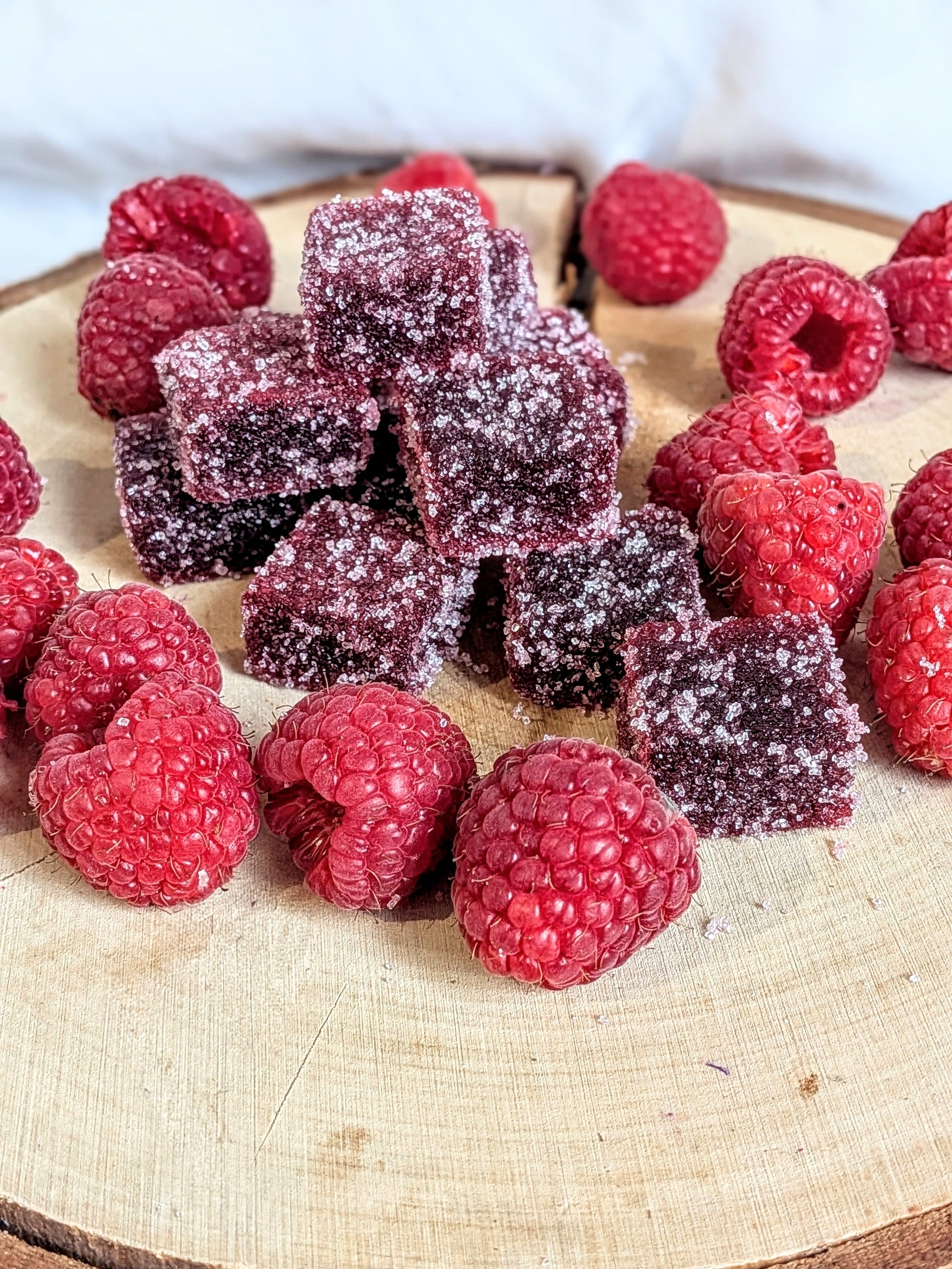 Pâtes de fruits artisanales à la framboise du Loiret disposées sur un socle en bois avec des framboises fraîches